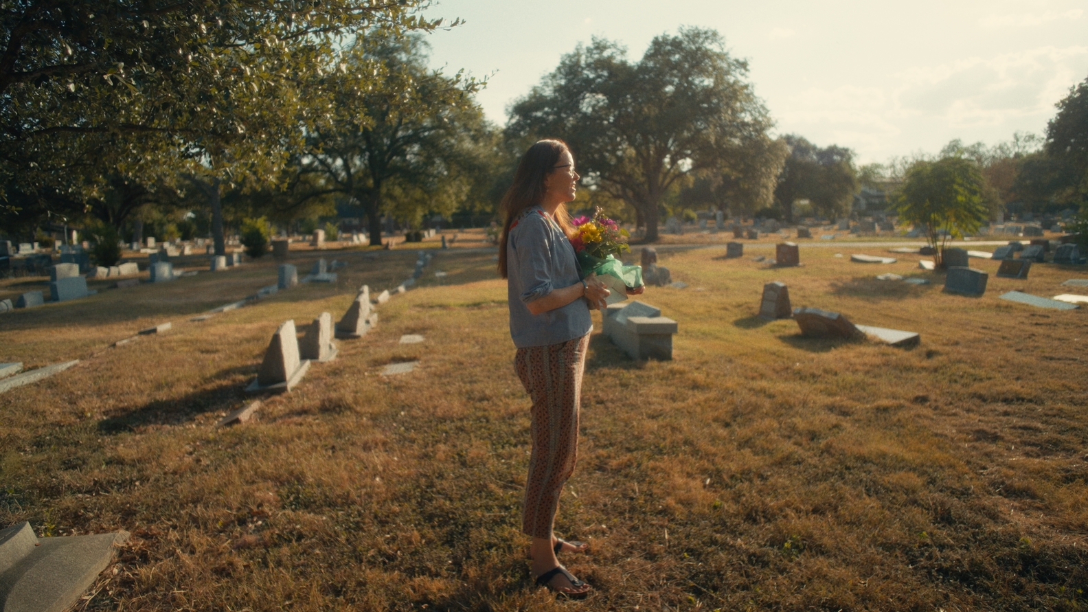 The Yogurt Shop Murders official HBO still: Sonora Thomas holding flowers in a sunlit cemetery.